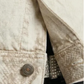 Close-up of a light beige textured denim jacket with a snakeskin-patterned cuff, paired with dark gray jeans and a studded belt.
