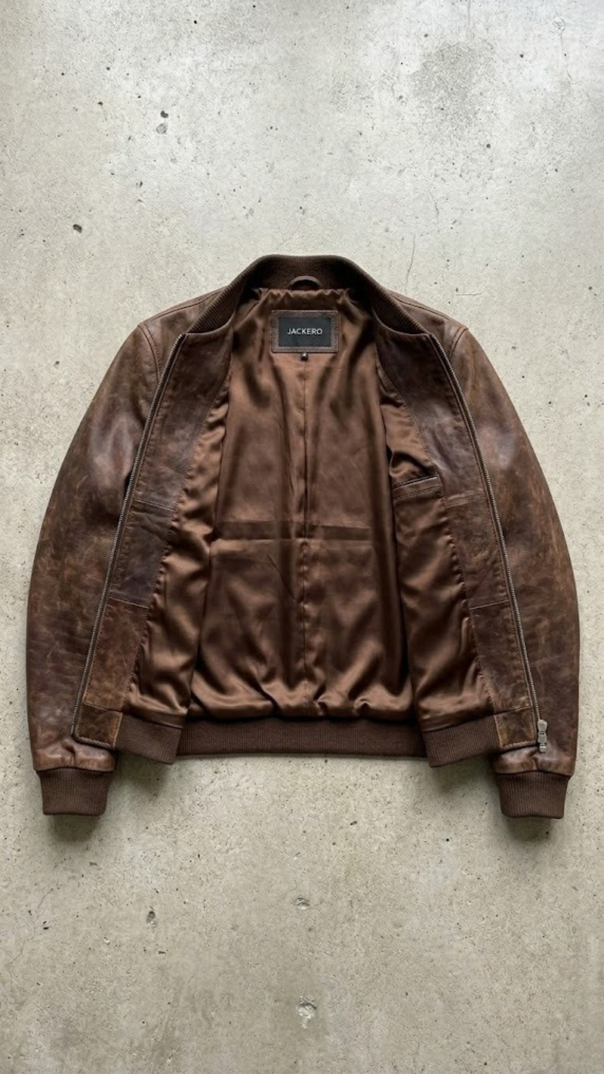 Professional studio product flat lay presentation featuring the genuine brown distressed leather casual bomber jacket neatly arranged on a clean backdrop.