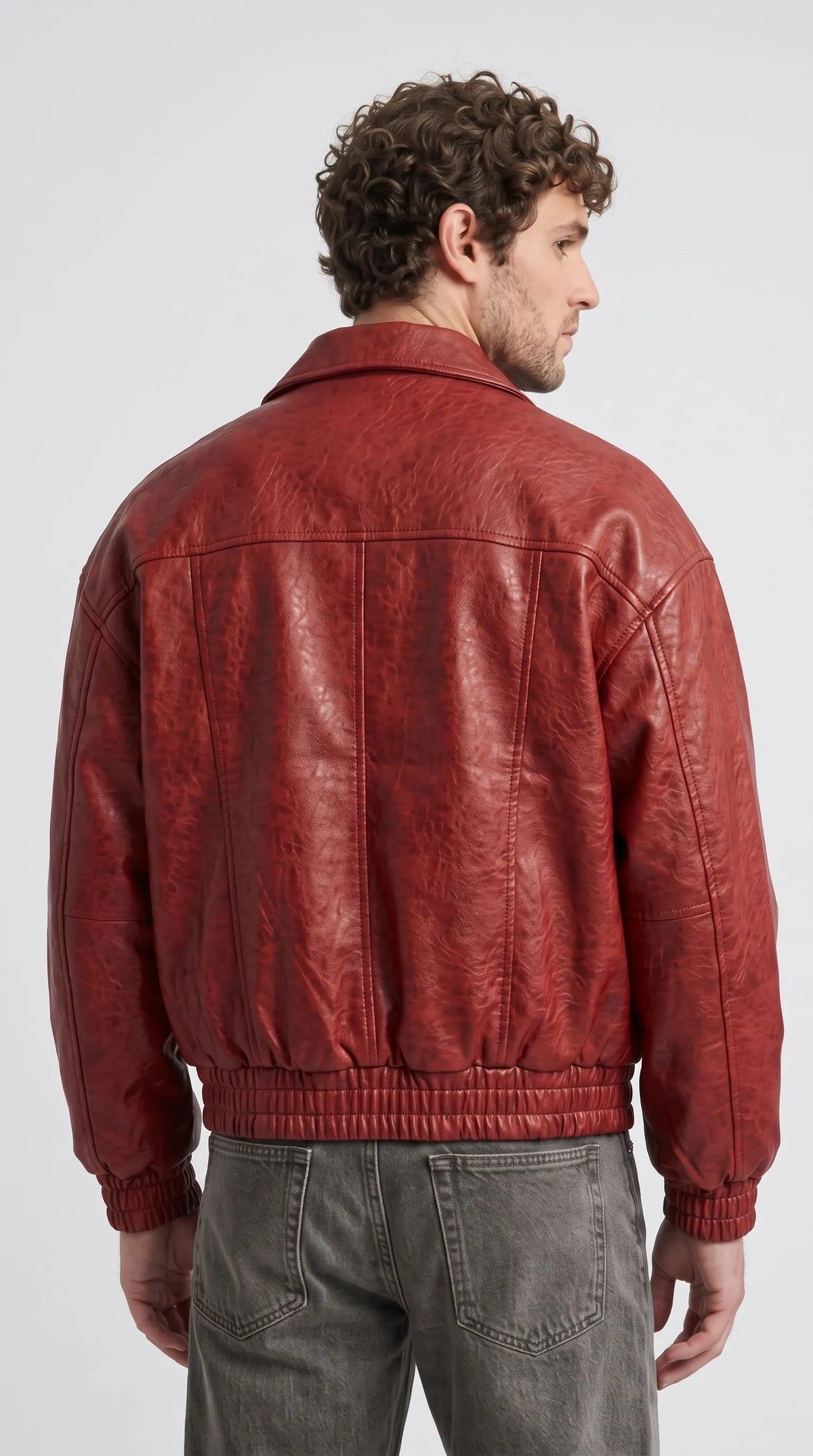 Model wearing a stylish red leather bomber jacket paired with men's vintage blue denim boot-cut jeans.