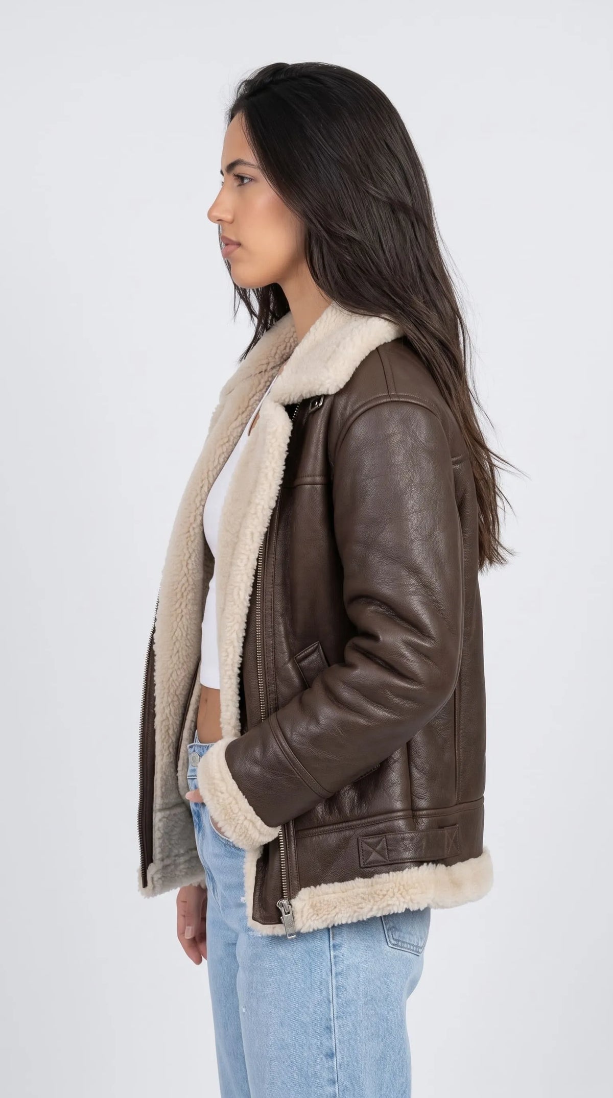 Oversized chocolate-brown leather aviator jacket with a generous off-white shearling collar, relaxed dropped shoulders, long sleeves and a shearling-edged waistband, styled with pale blue denim. The side silhouette shows the jacket’s roomy fit and textured leather panels, creating a laid-back vintage-inspired look that works with casual basics, denim outfits and contemporary cold-weather streetwear.