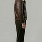 Minimalist catalog style photography of a premium dark brown leather outerwear coat with soft cream fur accents on a solid neutral background.