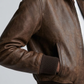 Detailed macro close-up shot capturing the heavy premium hide grain and rich espresso finish of the authentic dark brown leather bomber fabric.