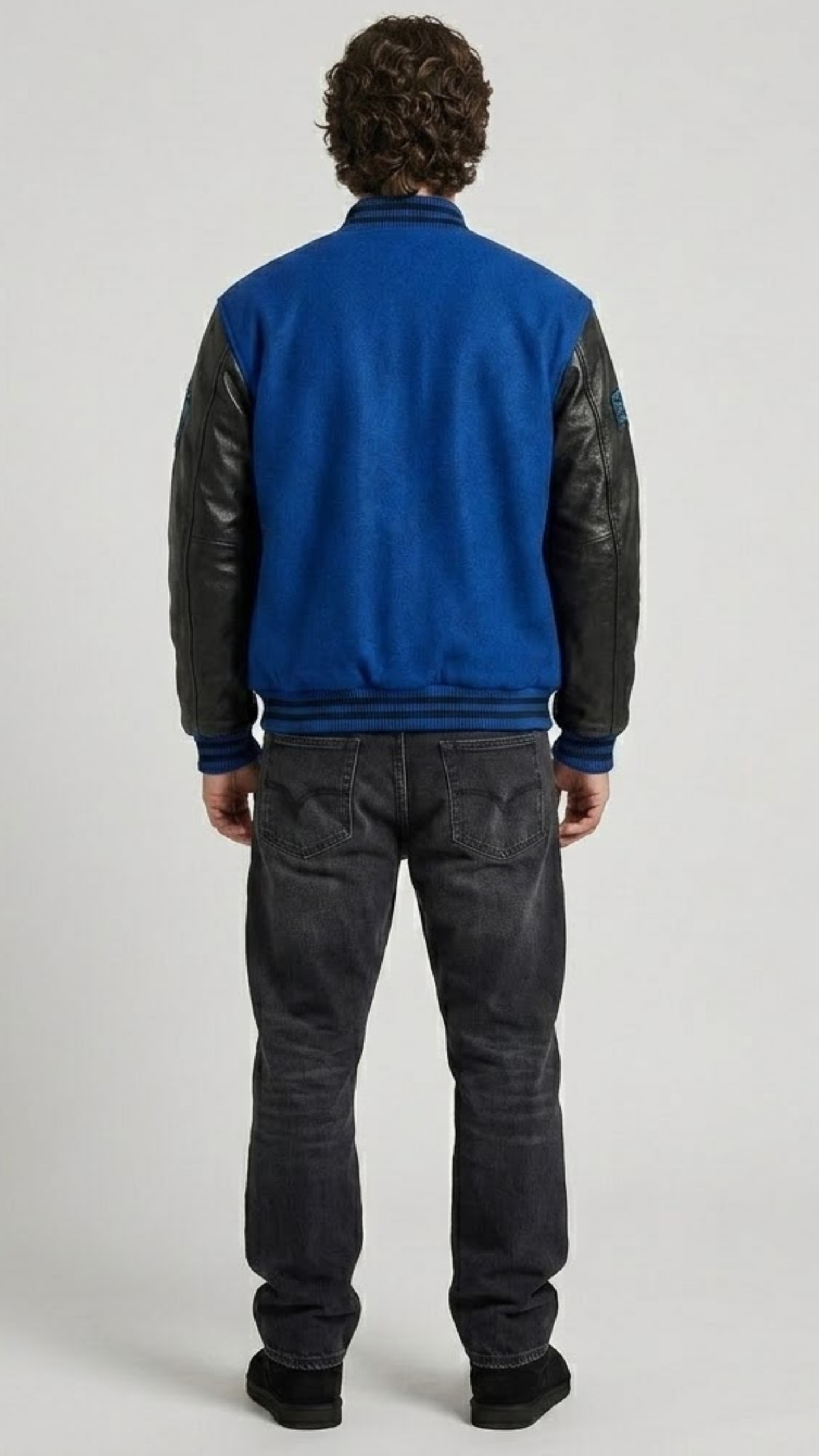 Detailed view of the athletic striped rib-knit collar, cuffs, and waistband on a premium blue suede varsity jacket.