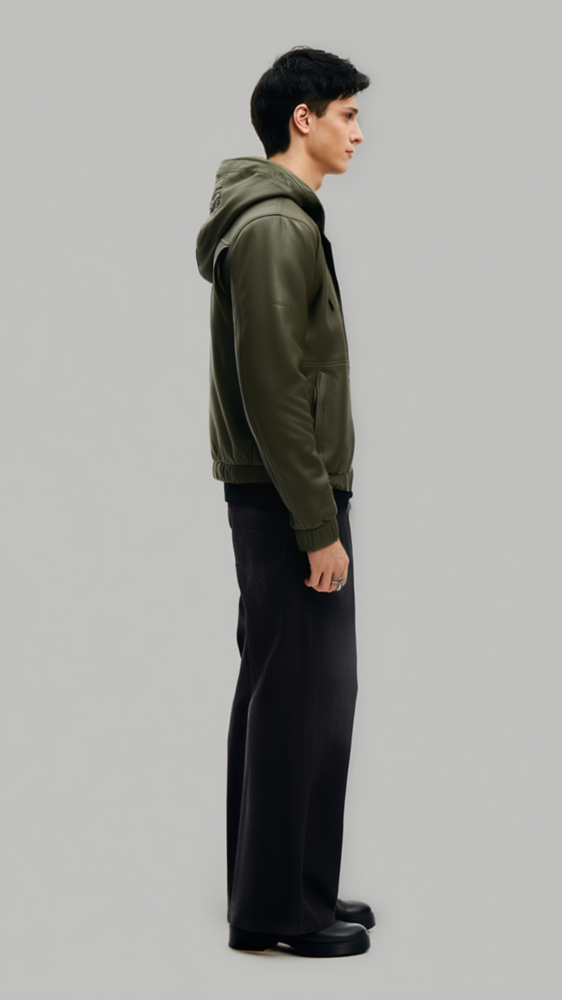 Model wearing a custom-fit dark green leather flight bomber jacket with a cozy shearling hood against a clean studio backdrop.