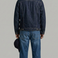 Person wearing a dark blue denim jacket and jeans on a gray background