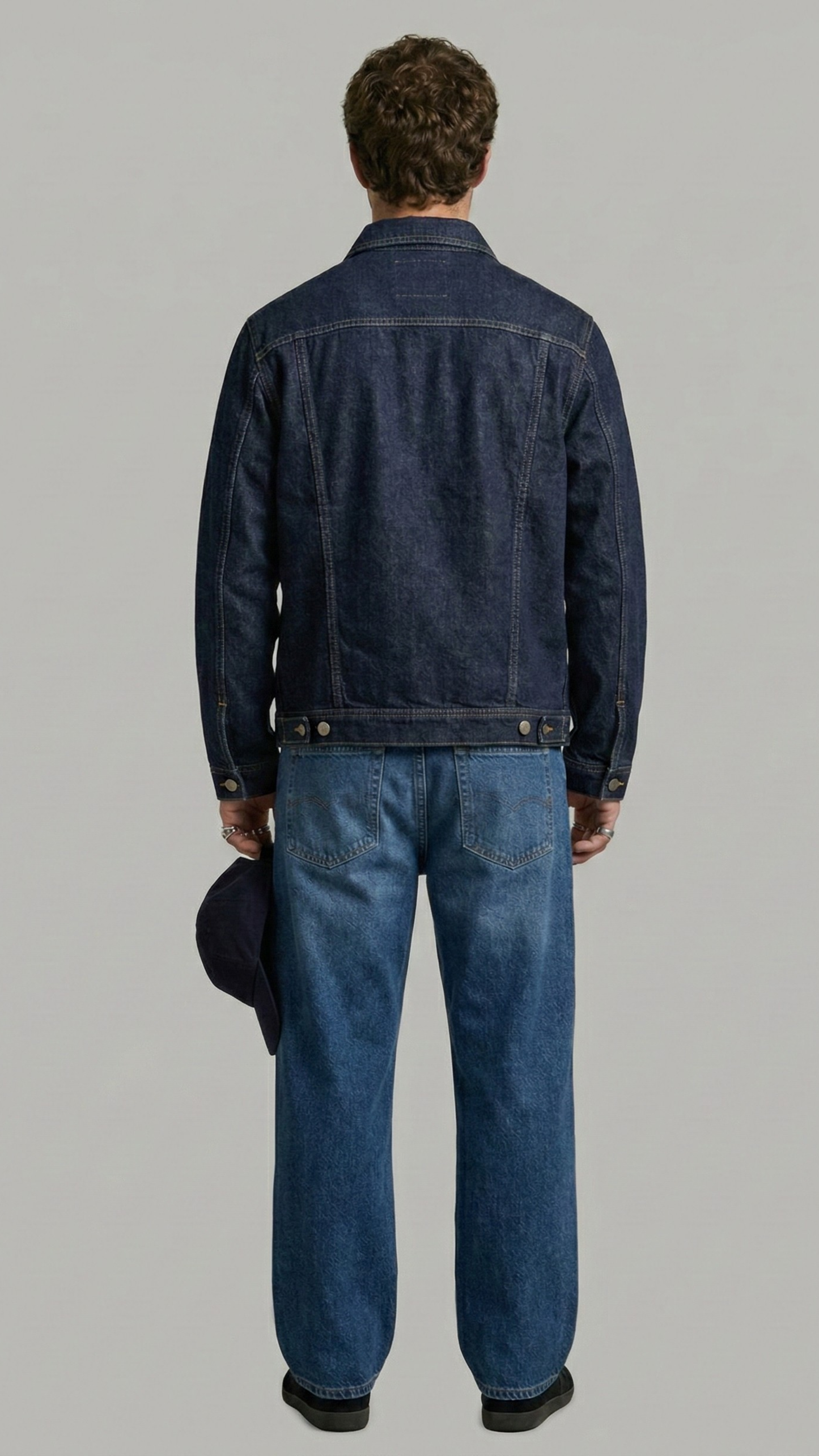 Person wearing a dark blue denim jacket and jeans on a gray background
