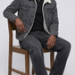 wearing a dark gray denim jacket with shearling, light olive pants, and off-white sneakers.