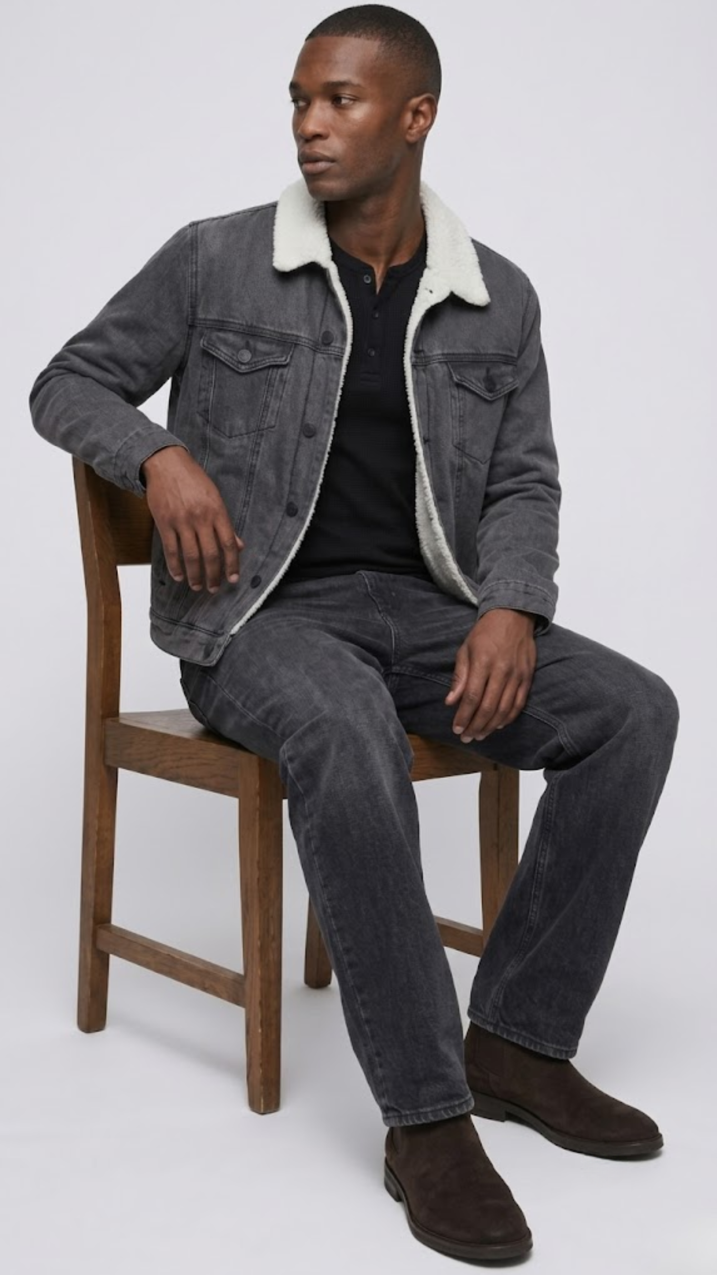 wearing a dark gray denim jacket with shearling, light olive pants, and off-white sneakers.