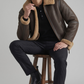 Full-body studio photography of a model showcasing a dark brown leather aviator coat with tan trim.