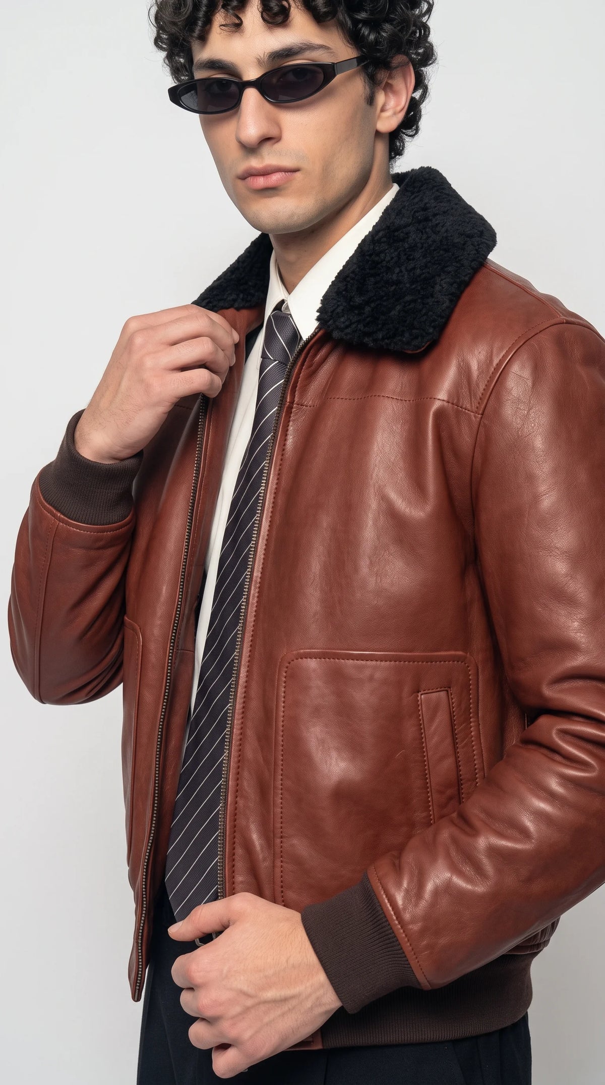 Close-up of a cognac-brown pebbled leather aviator jacket showcasing its rich tan grain texture, dense black faux-shearling collar, clean chest-panel stitching and metallic zipper teeth for a bold luxury flightwear aesthetic.