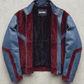 A color-blocked leather and suede jacket by Jackero, featuring blue leather sleeves and side panels, burgundy suede-like front and inner collar panels, and a black interior lining, laid flat on a textured gray concrete background.