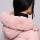 Person wearing a pink puffer coat with a fur-lined hood against a gray background