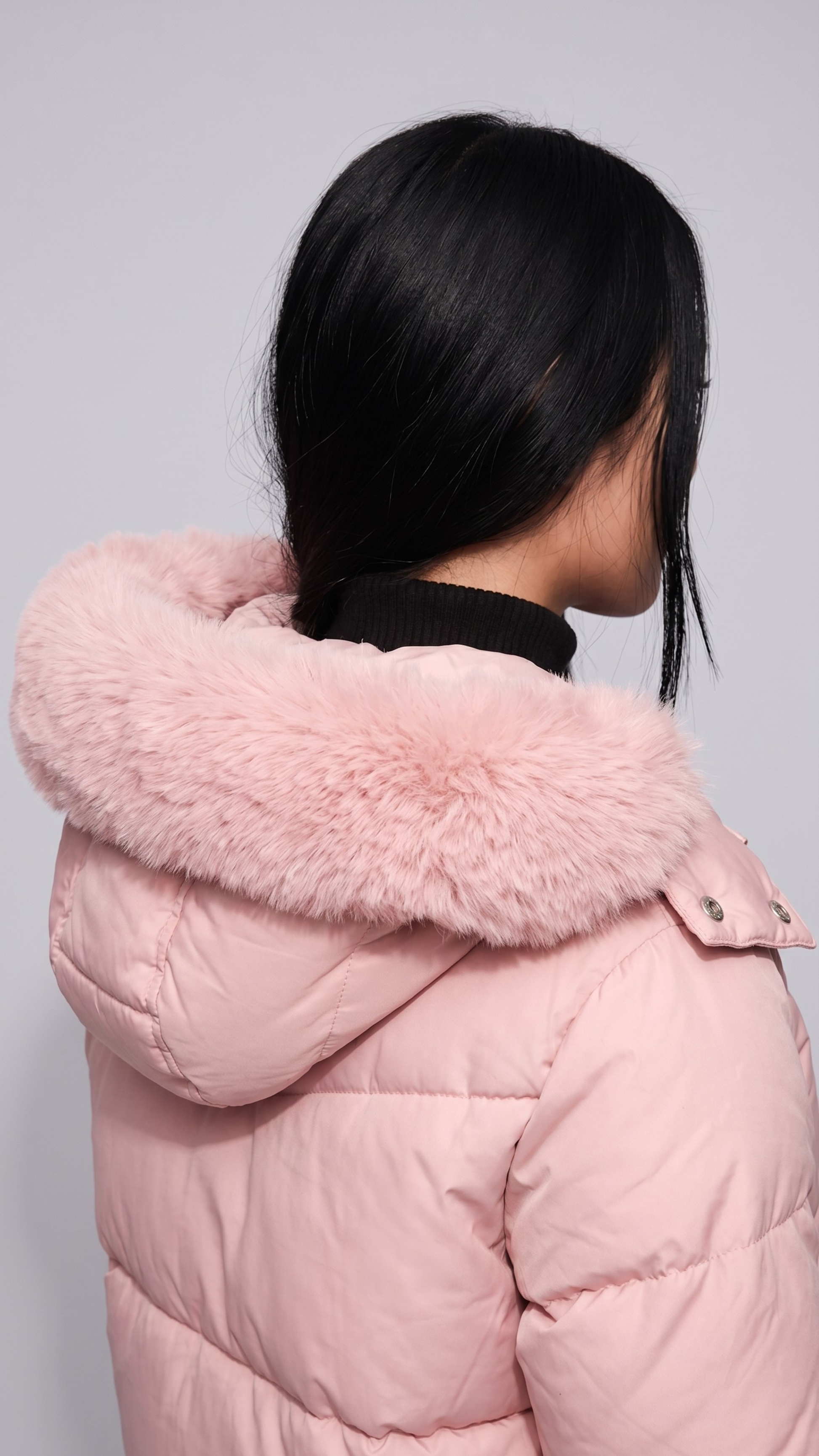 Person wearing a pink puffer coat with a fur-lined hood against a gray background