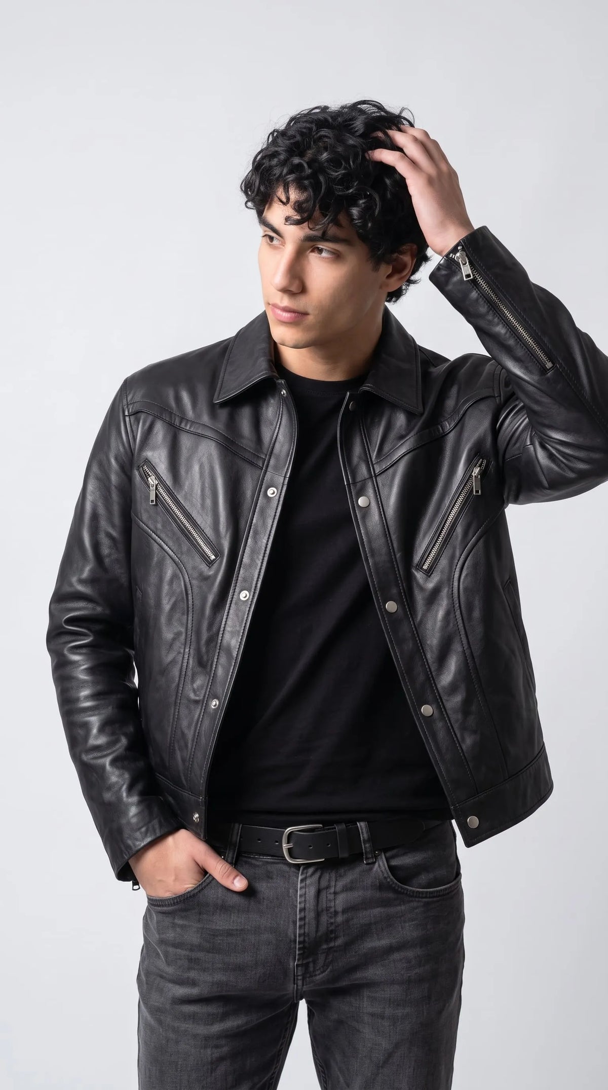 Men’s darkest black genuine leather baggy jacket styled over a plain black T-shirt with charcoal-grey jeans and a black leather belt. Its relaxed dropped-shoulder fit, curved front-panel stitching, pointed collar and silver snap-button placket create a bold contemporary moto-inspired outfit with an understated monochrome streetwear aesthetic.