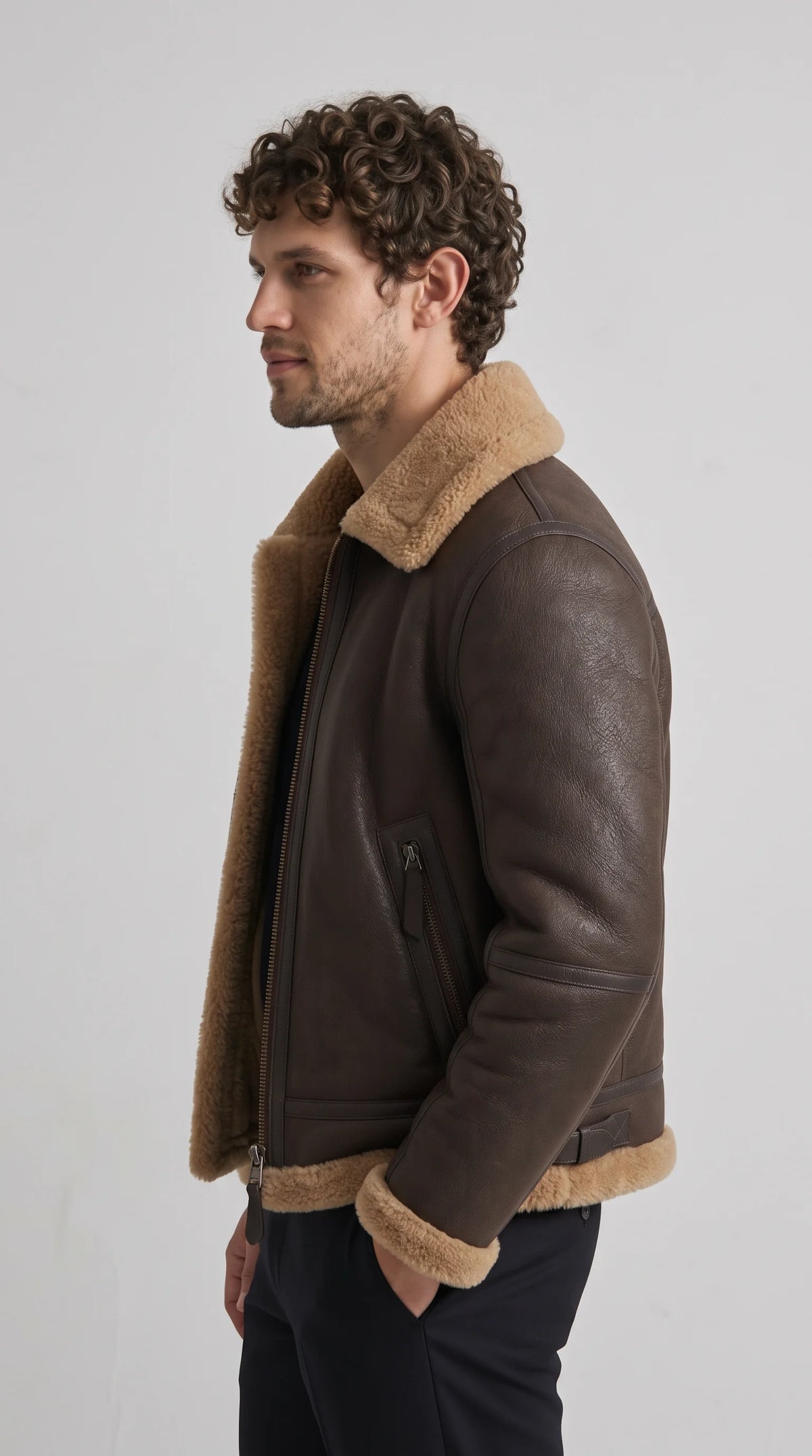 Dark brown leather aviator jacket with a sculpted shoulder, articulated sleeve seams, angled metal zip pockets and contrasting tan faux-shearling trim along the collar and hem, delivering a functional vintage flightwear look.