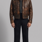 rugged dark brown distressed leather flight jacket with a thick cream shearling collar, standing against a clean grey studio backdrop.
