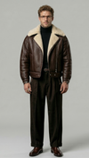 a model wearing a premium dark brown leather aviator jacket with a thick cream shearling collar, standing against a clean grey studio backdrop.