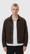 Dark espresso brown cotton canvas mechanic jacket with a classic pointed collar, antique brass-tone shank buttons and clean side slash pockets, styled over a white T-shirt for understated heritage workwear fashion.