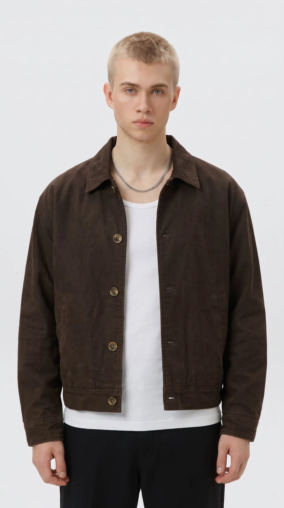 Dark espresso brown cotton canvas mechanic jacket with a classic pointed collar, antique brass-tone shank buttons and clean side slash pockets, styled over a white T-shirt for understated heritage workwear fashion.