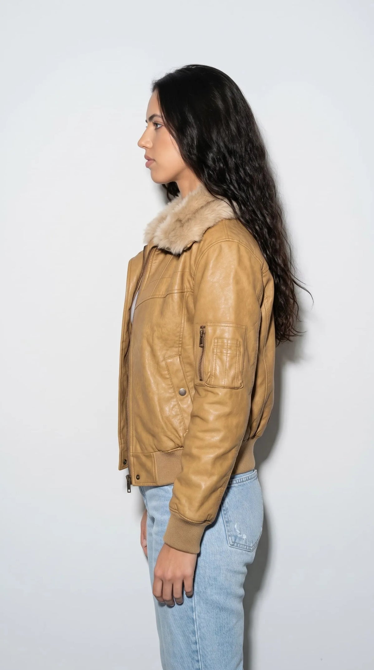 Dark mustard leather bomber jacket with a practical zippered sleeve pocket, textured gold-brown leather, a plush tan fur collar and snug ribbed cuffs. The sleeve hardware and carefully stitched panels introduce a functional aviation-inspired detail, while the cropped profile and warm colour make this jacket an eye-catching option for modern casual outfits and rugged-inspired street fashion.