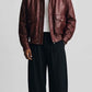 Front view of men wearing dark red oversized leather bomber jacket with full zip closure and ribbed collar.