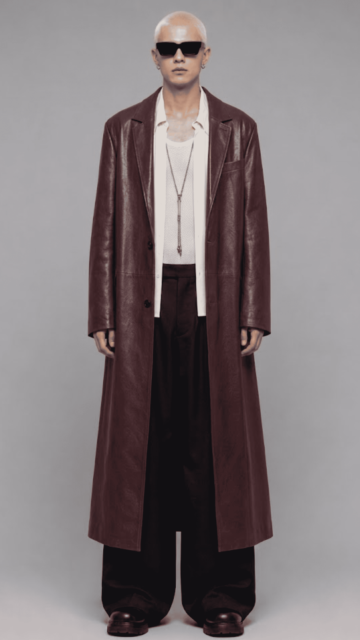 Full-length front view of model wearing an elegant dark red vine leather trench coat with a waist belt and button closure