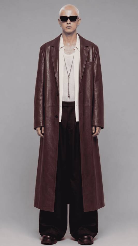 Full-length front view of model wearing an elegant dark red vine leather trench coat with a waist belt and button closure