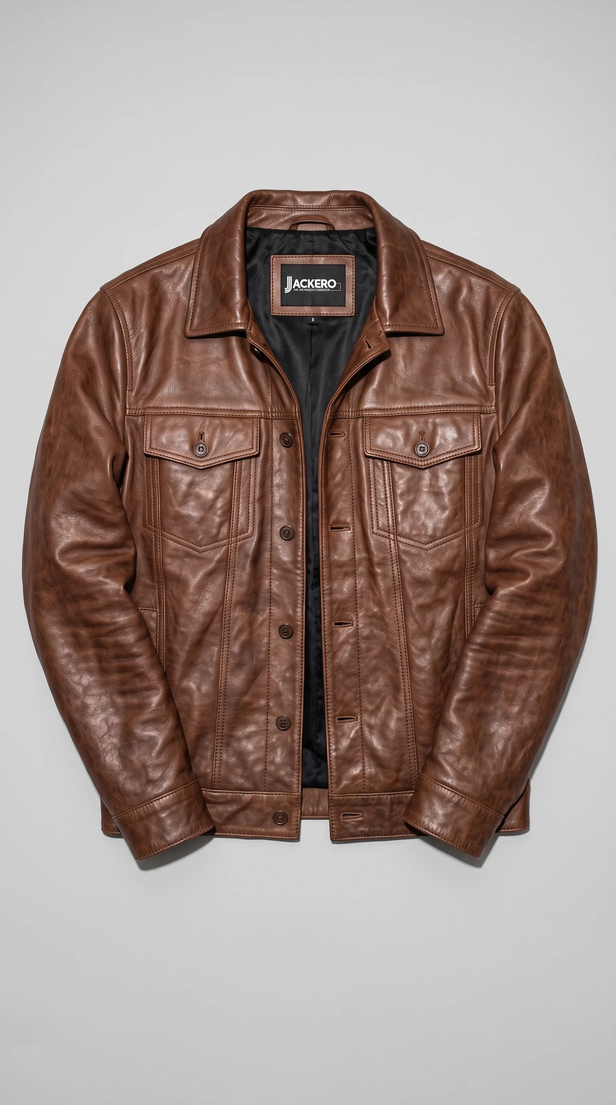 Dark tan brown distressed genuine leather jacket displayed open to reveal the JACKERO neck label and smooth interior lining, with custom metal shank buttons, twin flap chest pockets and clean vertical stitching completing its classic trucker-inspired design.