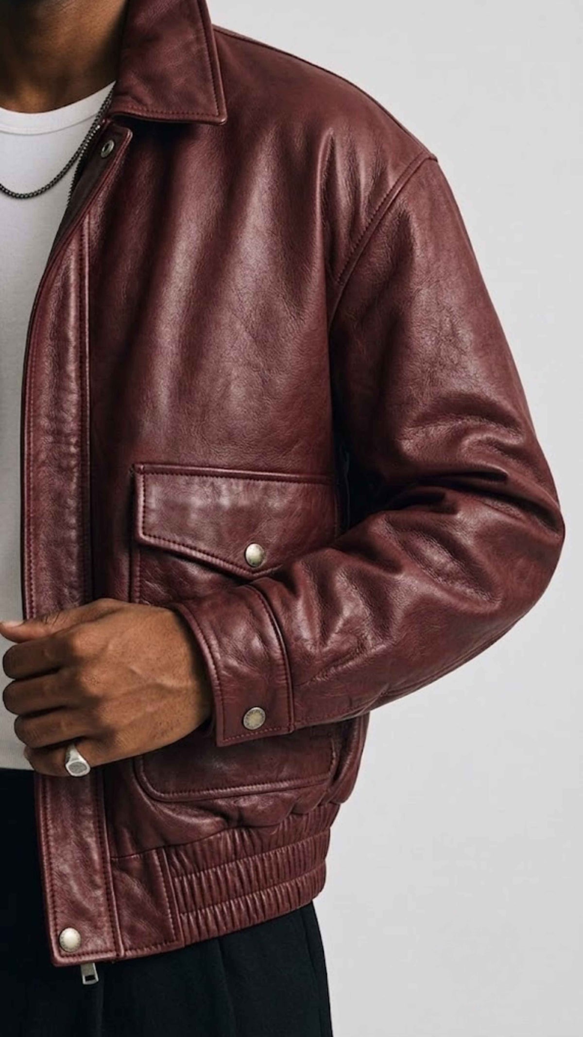 Close-up shot of rib-knit collar and heavy-duty front zipper on deep burgundy leather bomber jacket.