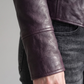 Macro detailed focus capture showing the fine premium grain texture and bold silver hardware accents on the dark violet leather jacket.