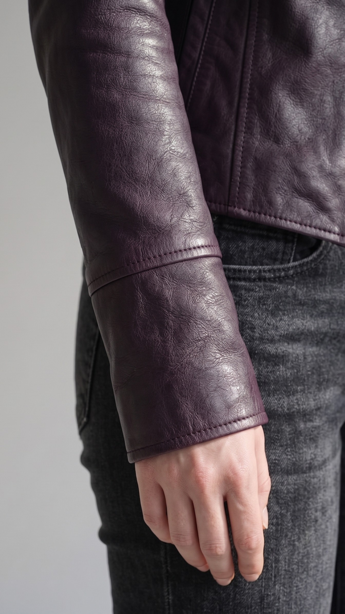 Macro detailed focus capture showing the fine premium grain texture and bold silver hardware accents on the dark violet leather jacket.