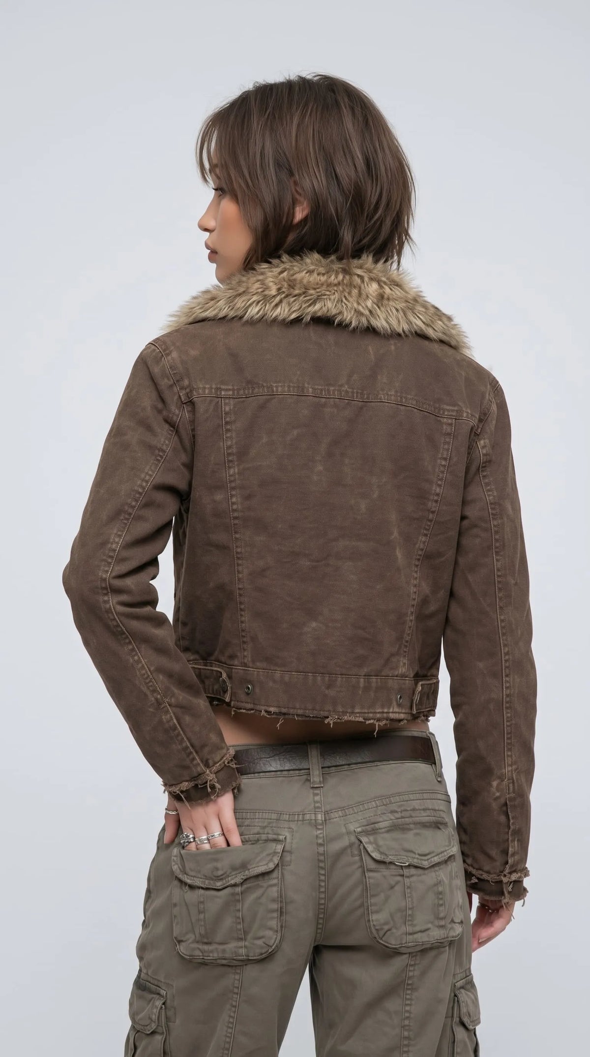 Dark khaki-brown cotton denim jacket with a broad plush tan faux-fur collar, structured upper-back yoke, visible panel stitching and an intentionally frayed cropped hem. Its washed, weathered finish gives the jacket a lived-in vintage character, while the clean back construction and rugged denim texture make it a distinctive layering piece for 1990s-inspired grunge outfits, casual cargo styling and alternative street fashion.