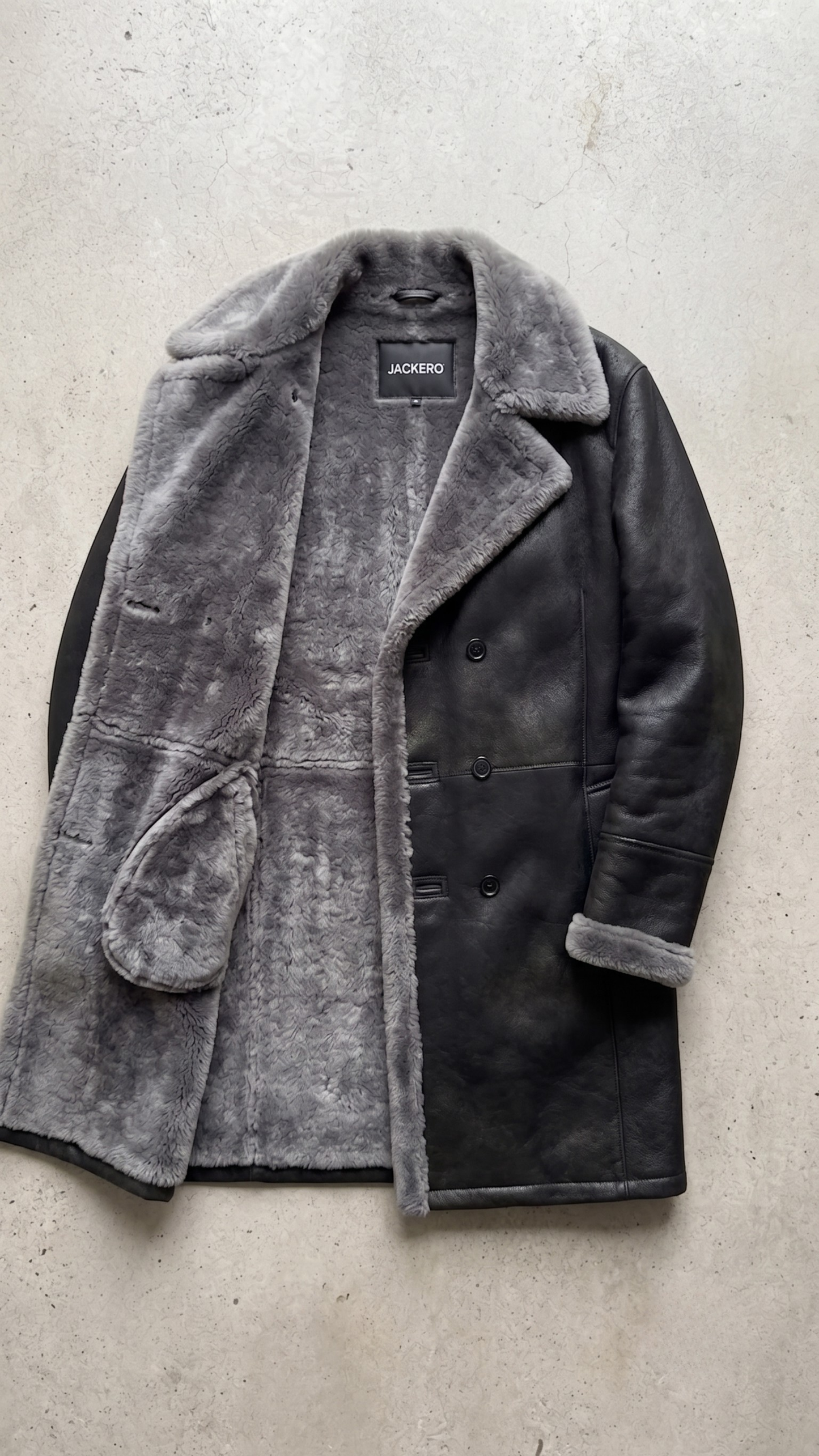 Detailed view of buttons and shearling trim on a high-quality men's dark grey leather coat.