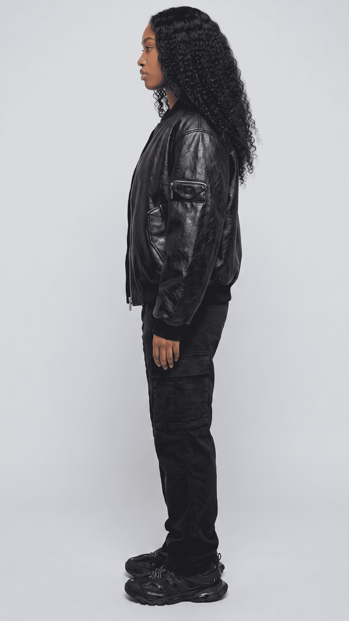 a model styled in a casual women's black leather bomber jacket with a clean t-shirt and sneakers.