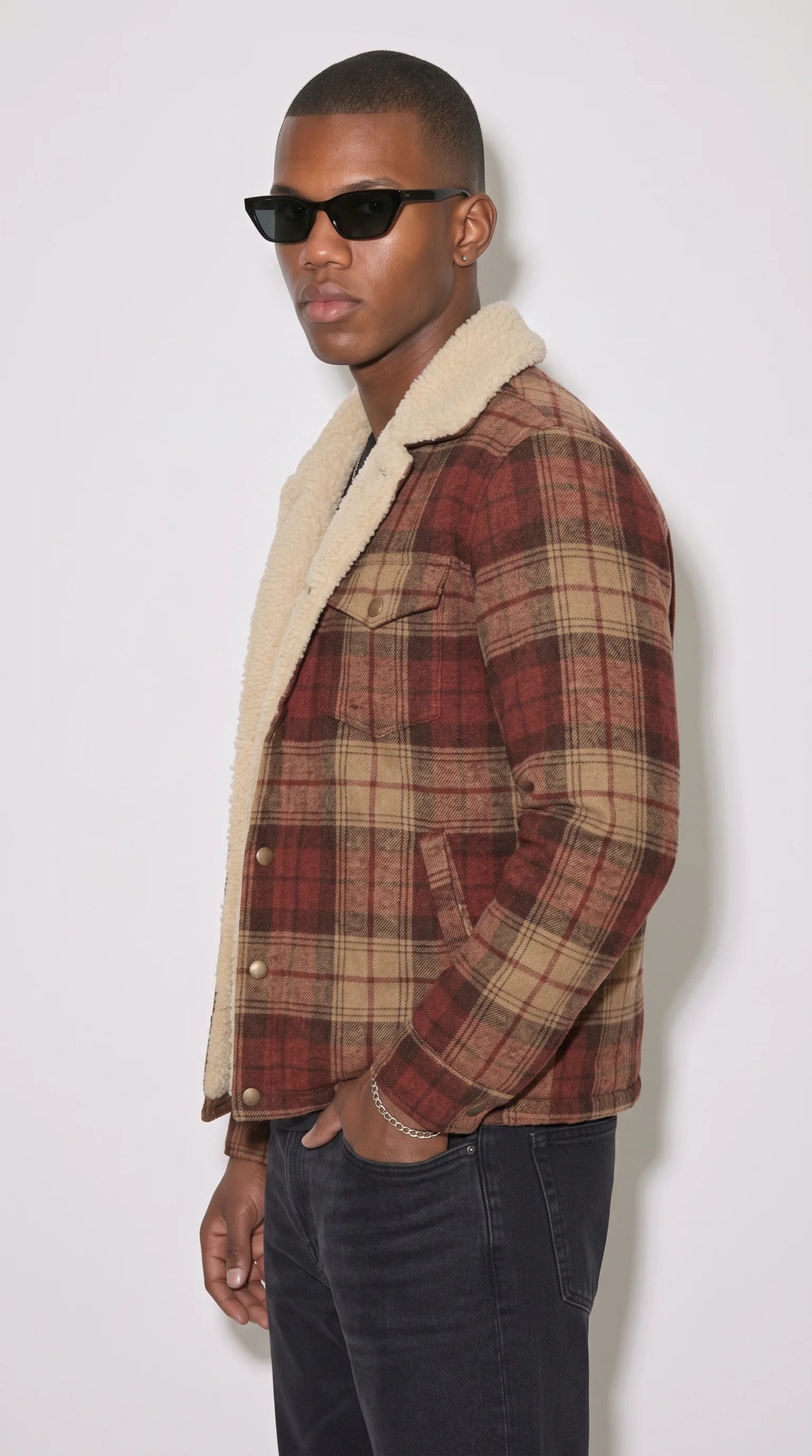 Earth-tone plaid cotton shacket with plush cream faux-shearling lining, styled with a black T-shirt and dark jeans in a relaxed studio editorial, showcasing the rust-red checked pattern, warm collar contrast and buttoned chest pockets for effortless cold-weather fashion.