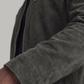 Close-up of a person wearing a dark gray suede jacket, showing the sleeve with a snap button and a zippered chest pocket.