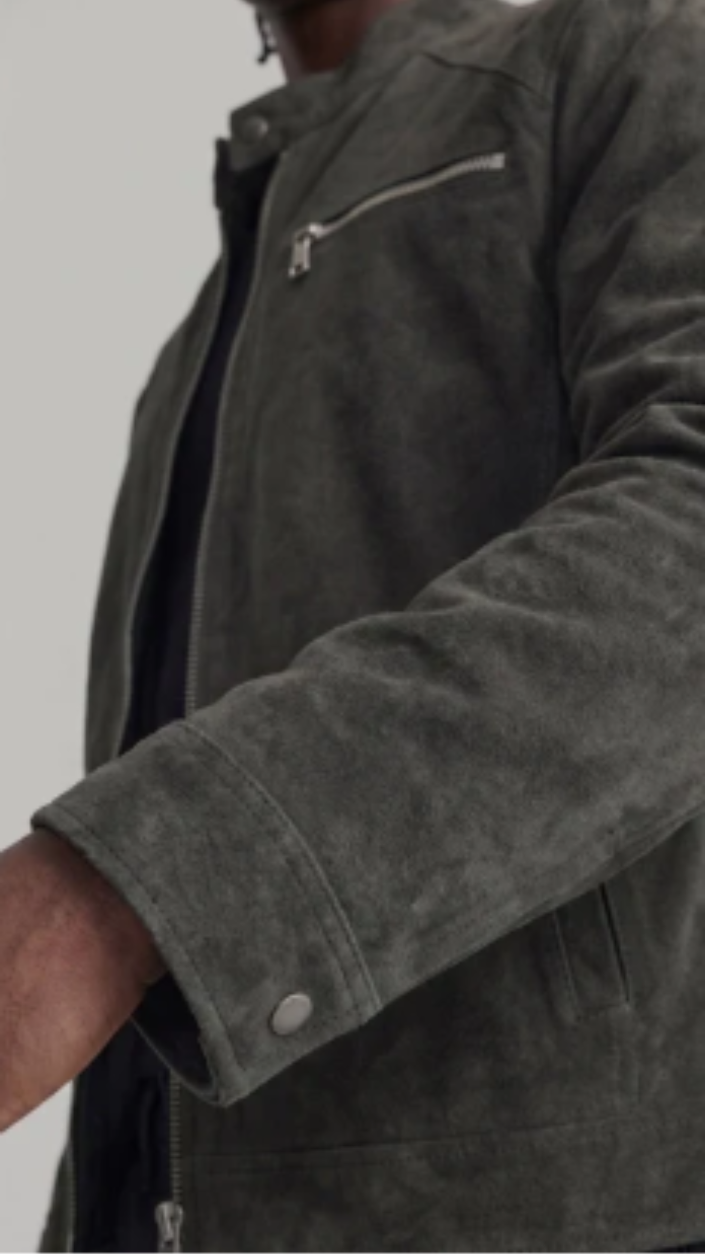 Close-up of a person wearing a dark gray suede jacket, showing the sleeve with a snap button and a zippered chest pocket.