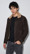 A dark chocolate brown genuine suede jacket features a thick cream shearling-lined pointed collar, textured matte leather and a full-length metallic front zipper. The striking contrast between rich espresso tones and plush ivory pile creates a sophisticated winter outerwear statement for men seeking elevated casual fashion, premium layering and modern cold-weather style.