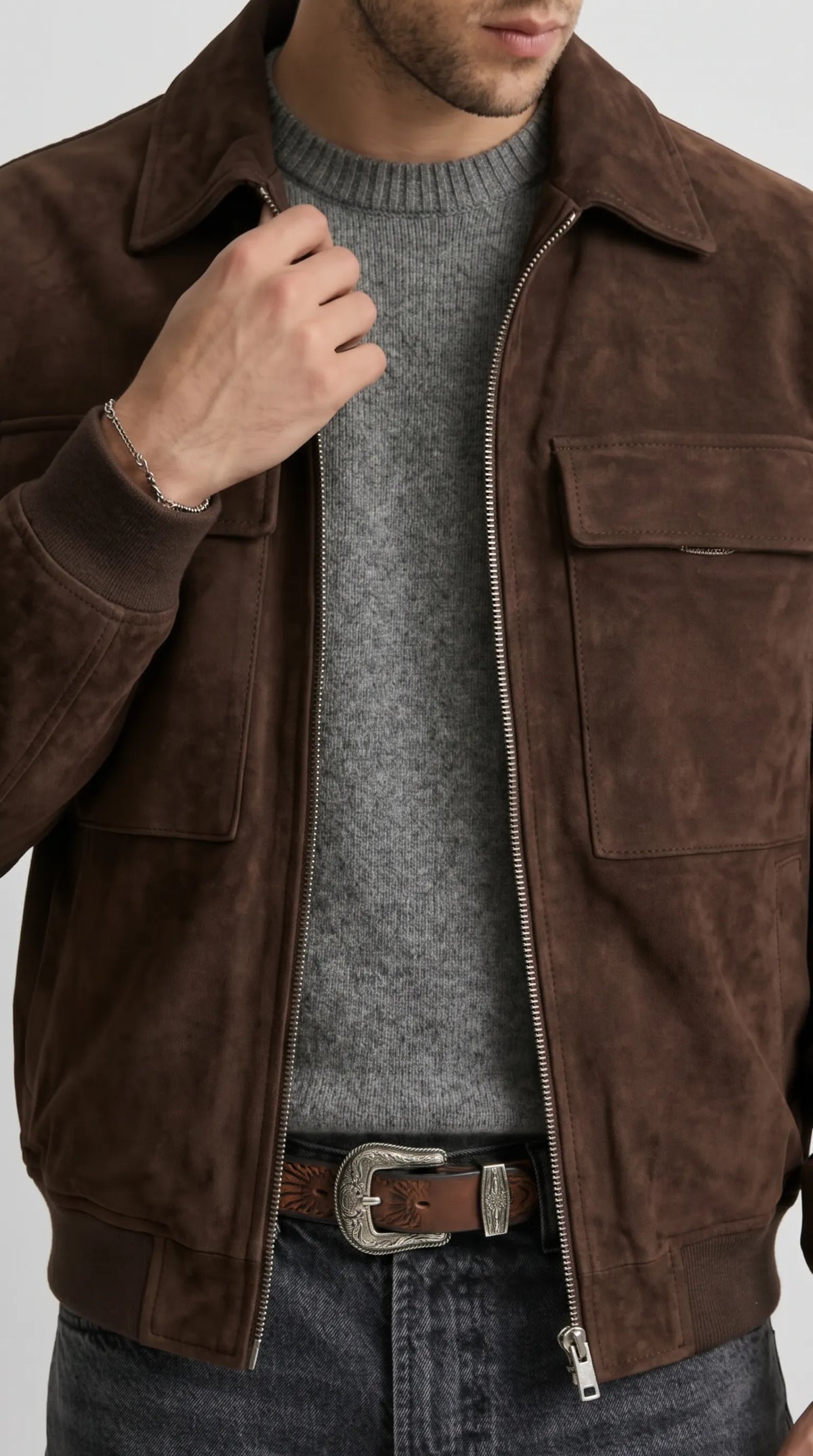 Close-up detail of a dark chocolate suede jacket highlighting its classic point collar, custom metal front zipper and deep side welt pockets. The soft, velvety suede surface gives the rich espresso-brown colour subtle depth, while the uncluttered hardware and clean construction create a refined alternative to a conventional casual bomber jacket.