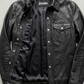 Jackero jacket flat lay photography of a high-end black leather shirt-style trucker coat displayed on a solid grey backdrop.