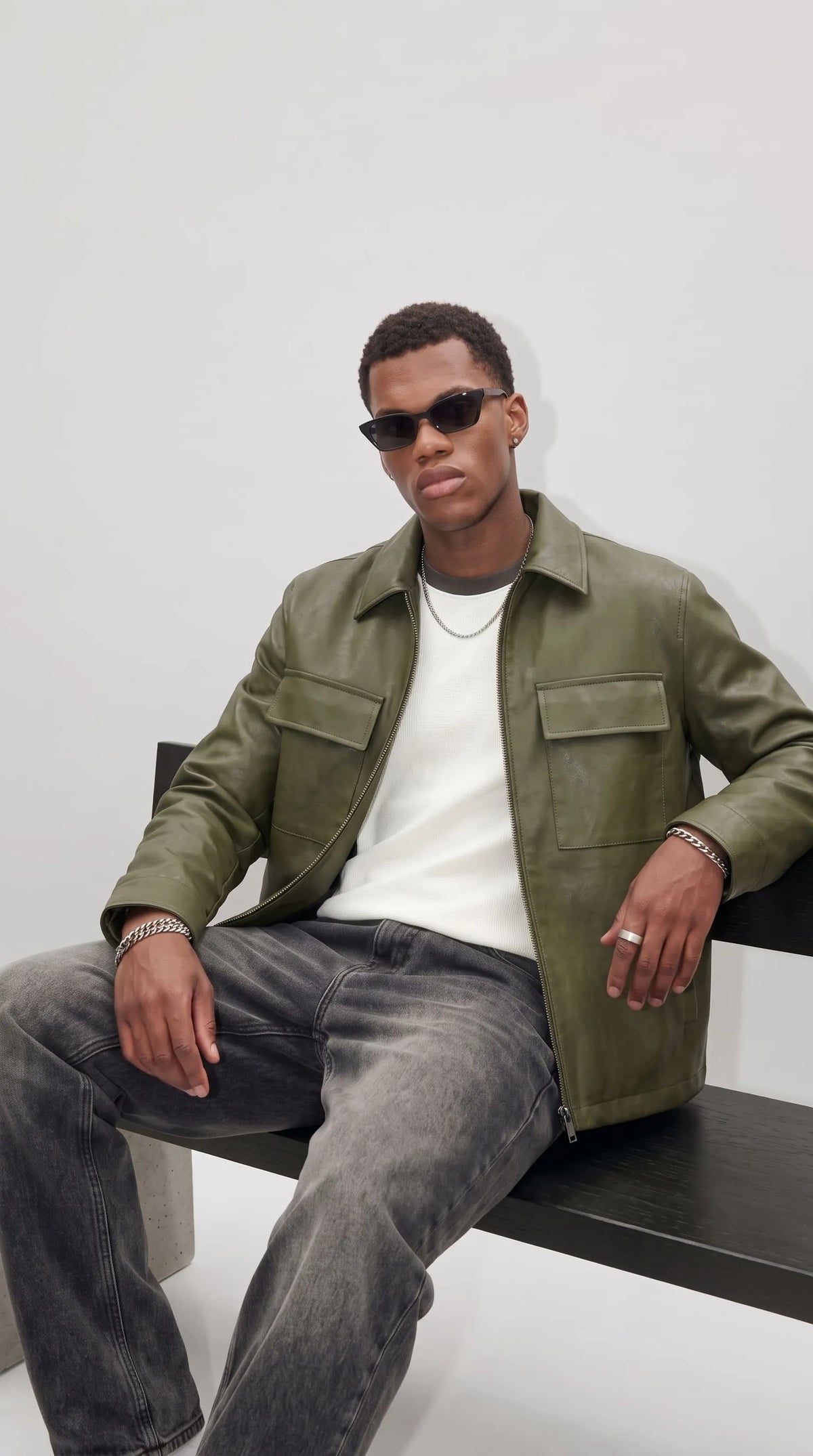 Casual men's outfit idea: olive green leather jacket layered over a white t-shirt with grey ribbed crew neck