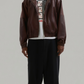 Premium dark maroon leather bomber jacket with an adjustable drawstring hood, featuring front zip closure and ribbed cuffs by Jackero.
