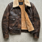 Brown leather jacket with beige fur lining on a gray concrete surface