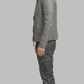 A man shown in profile wearing a gray leather jacket, dark gray cargo jeans, and brown boots, standing against a solid gray background.