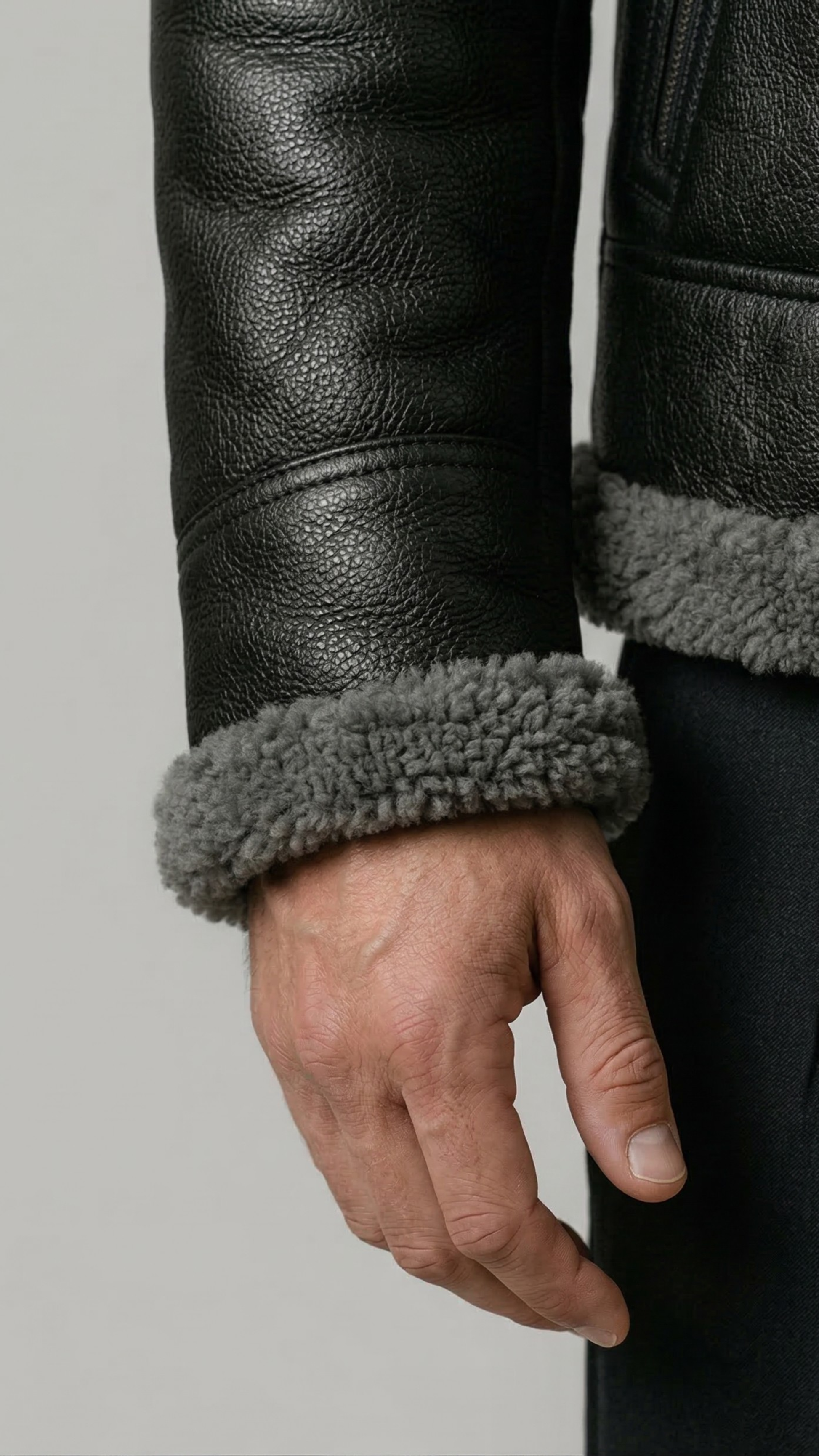 Close-up of a black leather jacket with gray fur lining on a plain background