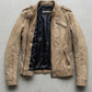 A cropped brown faux leather jacket with cream-colored diagonal stripes on the chest and sleeves, laid flat on a textured gray concrete surface. The brand name 'JACKERO' is visible on the inner neck label.