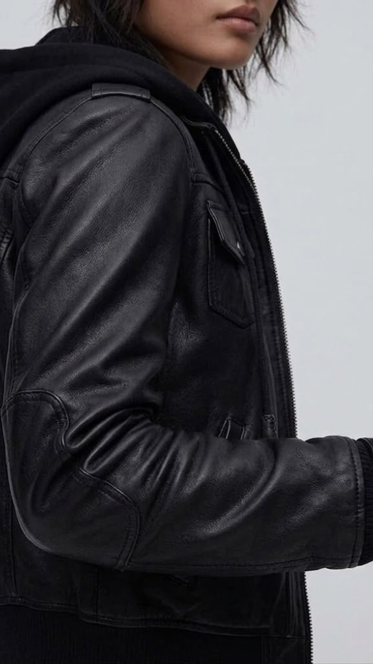 Macro detailed focus capture showing the rich grain sheen of the black genuine leather jacket and tactile adjustable hood details.