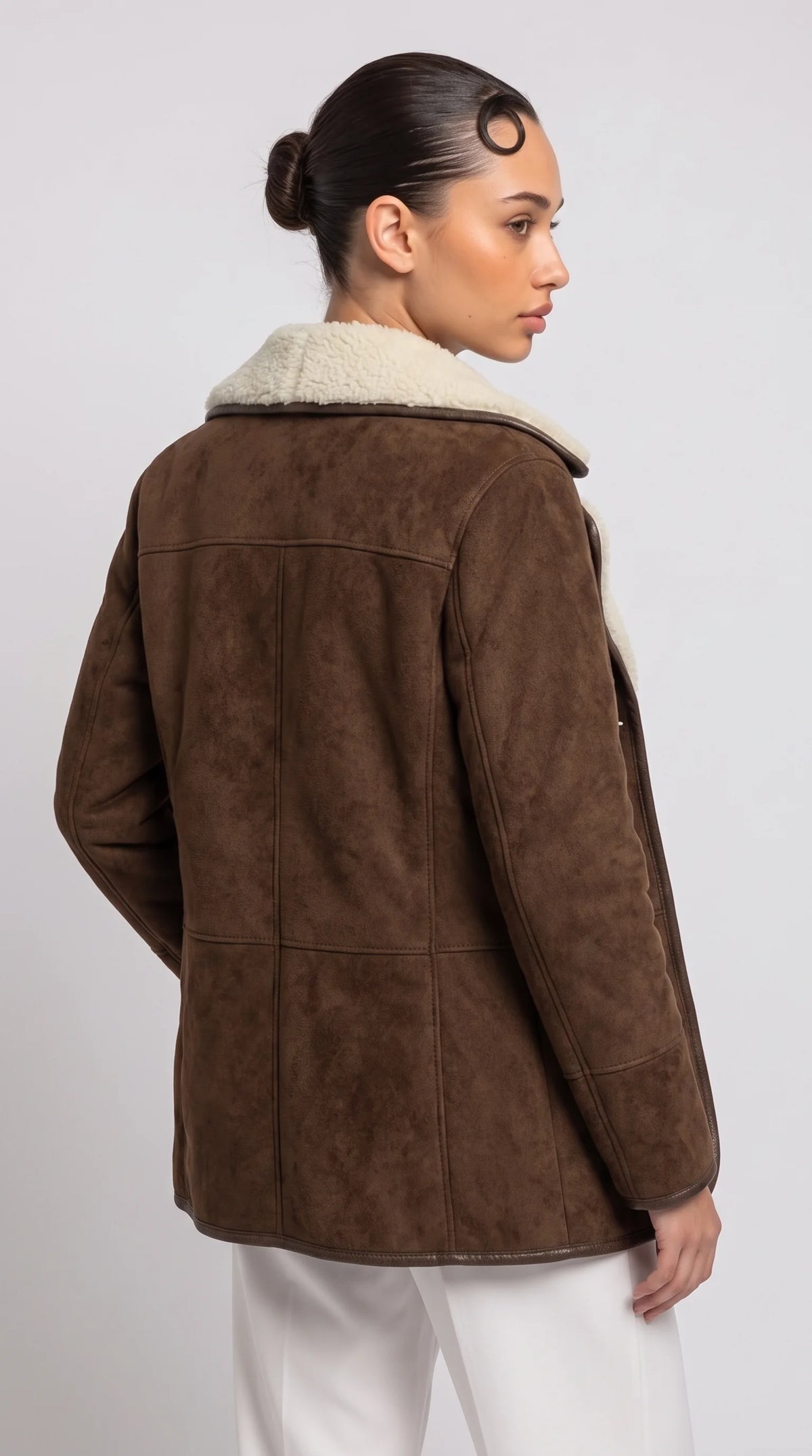 Heritage-inspired dark brown suede aviator coat featuring a horizontal shoulder yoke, clean vertical back-panel seams, long suede sleeves and a wide cream faux-shearling collar, highlighting its understated construction and elegant straight silhouette for timeless winter outerwear.