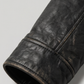 Close-up micro detail focusing on the premium zippered chest pockets and ribbed cuffs of a black leather hooded coat.