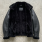 Warm black leather flight jacket with thick shearling collar on a light grey studio background.